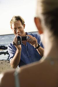 Smiling Man Filming Woman At Beach