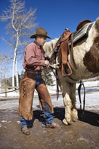 Cowboy Putting Saddle on Horse