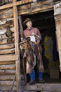 Man Wearing Cowboy Hat Holding a Saddle