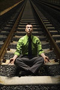 Businessman Meditating on Railroad Tracks.