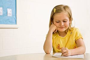 Young Girl Smiling in Classroom Writing on Paper