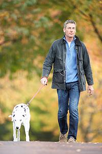 Man Walking Dog Through Autumn Park Listening to MP3 Player