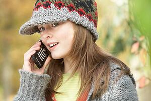 Head And Shoulders Of Young Girl In Autumn Woodland Using Mobile Phone