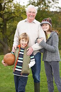 Grandfather With Grandchildren Holding Football Outside