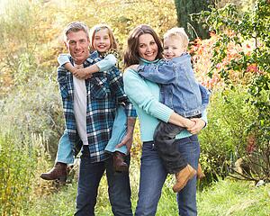 Family Group Outdoors In Autumn Landscape With Parents Giving Chiildren Piggyback