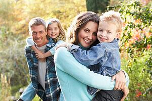 Family Group Outdoors In Autumn Landscape With Parents Giving Chiildren Piggyback