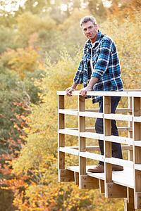 Man Standing On Wooden Balcony Overlooking Autumn Woodland