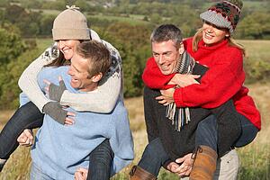 Two Couples Having Piggyback Ride In Autumn Landscape