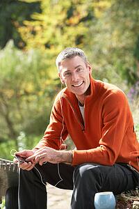 Man Outdoors Listening To MP3 Player Whilst On Break From Gardening