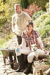 Couple With Dog Having Coffee Break Whilst Working Outdoors In Garden