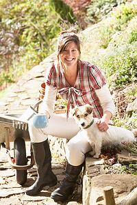 Woman With Dog Having Coffee Break Whilst Working Outdoors In Garden