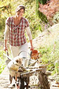 Woman With Dog Having Coffee Break Whilst Working Outdoors In Garden