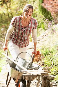 Woman With Wheelbarrow Working Outdoors In Garden