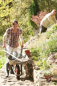 Couple With Wheelbarrow Working Outdoors In Garden