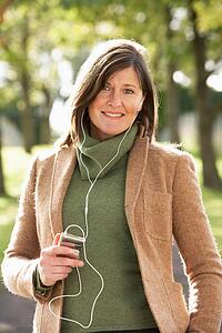 Woman Listening To MP3 Whilst Walking In Autumn Park