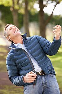 Man Listening To MP3 Whilst Walking In Autumn Park