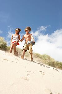 Young Couple Running Down Sand Dune On Beach