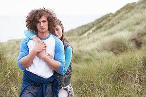 Young Couple Walking Through Sand Dunes Wearing Warm Clothing