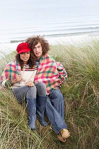 Young Couple Sitting In Sand Dunes Wrapped In Blanket