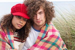 Young Couple Sitting In Sand Dunes Wrapped In Blanket