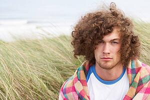 Young Man Standing In Sand Dunes Wrapped In Blanket