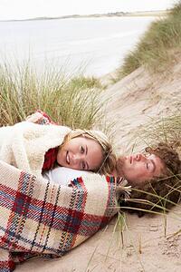 Teenage Couple Sitting In Sand Dunes Wrapped In Blanket