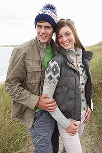 Young Couple Walking Through Sand Dunes Wearing Warm Clothing