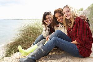 Three Teenage Girls Sitting In Sand Dunes Together
