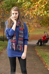 Unhappy Teenage Girl Standing In Autumn Park With Couple On Bench In Background