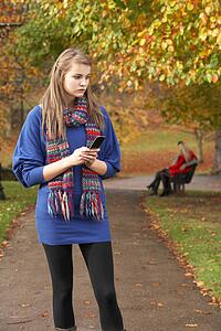 Unhappy Teenage Girl Standing In Autumn Park With Couple On Bench In Background
