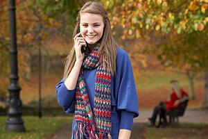 Teenage Girl On Mobile Phone In Autumn Park With Couple On Bench In Background