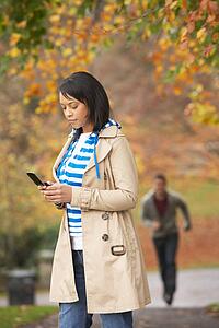 Teenage Girl Making Mobile Phone Call With Boyfriend Running Towards Her In Background
