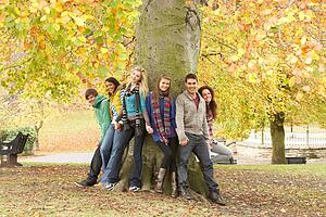 Group Of Six Teenage Friends Leaning Against Tree In Autumn Park