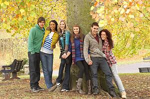 Group Of Six Teenage Friends Leaning Against Tree In Autumn Park