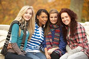 Group Of Four Teenage Girls Sitting On Bench In Autumn Park
