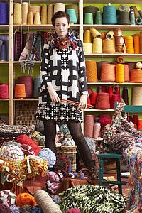 Woman Holding Knitting Needles Standing In Front Of Yarn Display