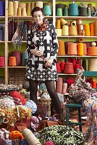Woman Holding Knitting Needles Standing In Front Of Yarn Display