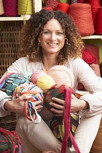 Woman Holding Balls Of Wool Sitting In Front Of Yarn Display