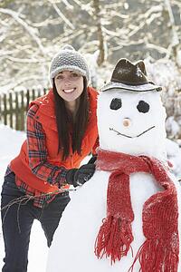 Young Woman Building Snowman In Garden