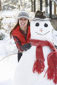 Young Woman Building Snowman In Garden