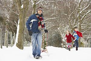 Father Pulling Children On Sledge Through Winter Landscape