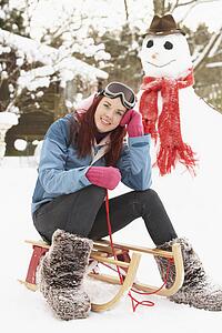 Teenage Girl With Sledge Next To Snowman