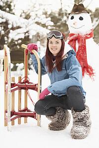 Teenage Girl With Sledge Next To Snowman