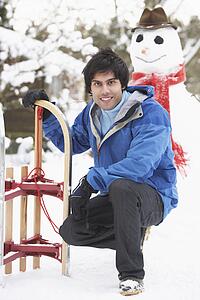Teenage Boy With Sledge Next To Snowman