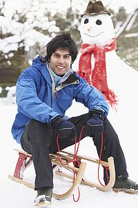 Teenage Boy With Sledge Next To Snowman