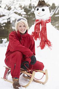 Teenage Girl With Sledge Next To Snowman