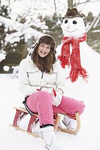 Teenage Girl With Sledge Next To Snowman