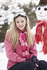 Teenage Girl With Sledge Next To Snowman