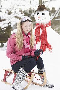 Teenage Girl With Sledge Next To Snowman