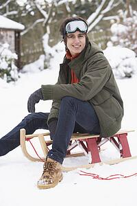 Teenage Boy With Sledge Next To Snowman